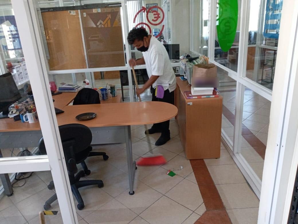 Colaborador barriendo el piso de una oficina con divisiones de cristal