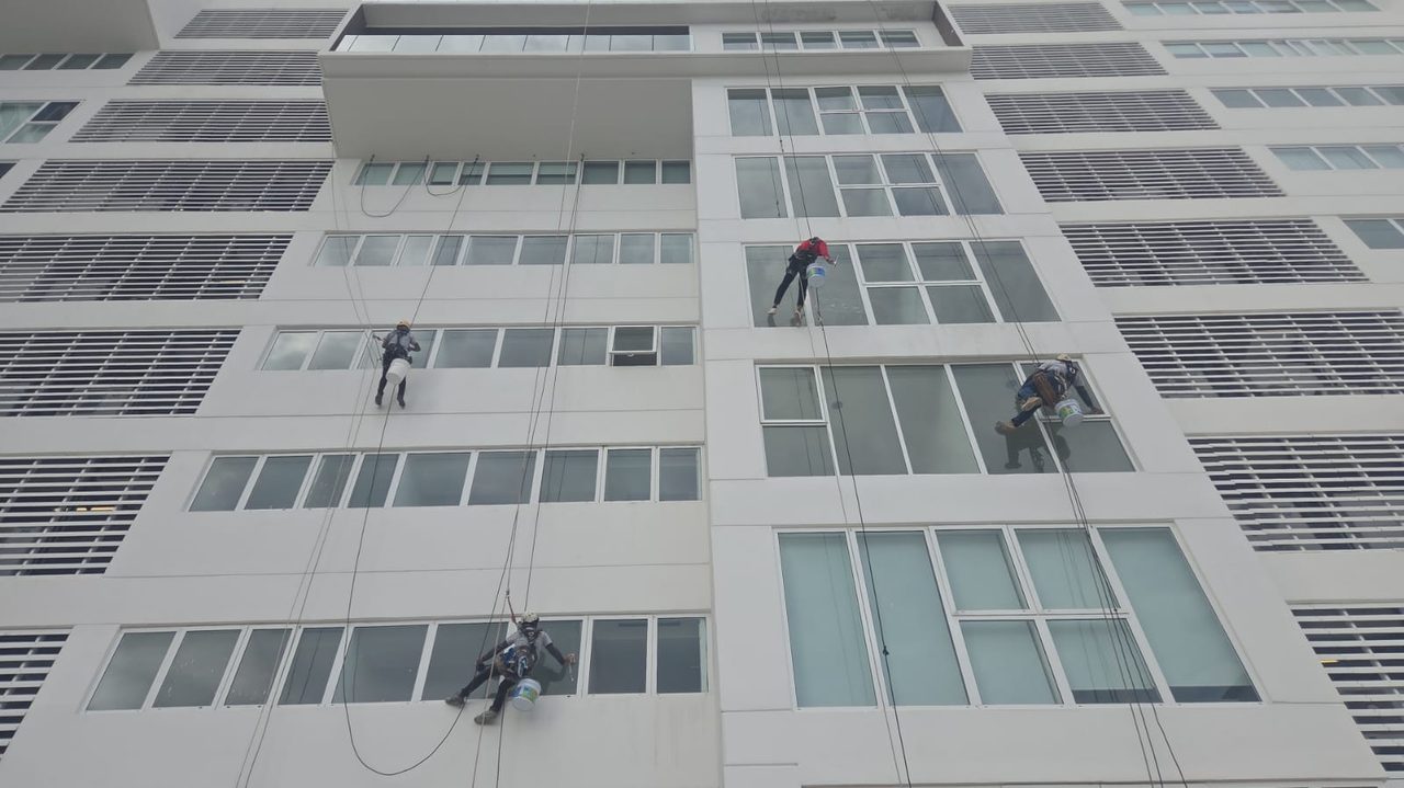 Cuatro técnicos suspendidos con cuerdas limpiando los cristales de la fachada de un edificio